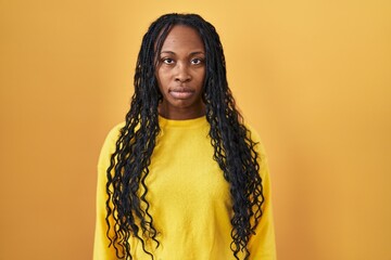 Sticker - African woman standing over yellow background relaxed with serious expression on face. simple and natural looking at the camera.