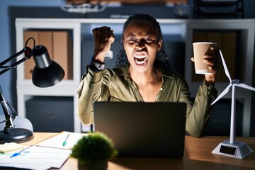 Canvas Print - African woman working using computer laptop at night angry and mad raising fist frustrated and furious while shouting with anger. rage and aggressive concept.