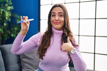 Canvas Print - Young brunette woman holding pregnancy test result pointing finger to one self smiling happy and proud