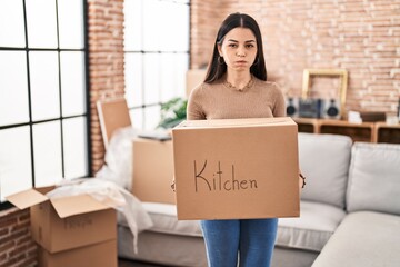 Wall Mural - Young woman moving to a new home holding box puffing cheeks with funny face. mouth inflated with air, catching air.