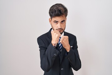 Sticker - Young hispanic man with tattoos wearing business suit and tie ready to fight with fist defense gesture, angry and upset face, afraid of problem