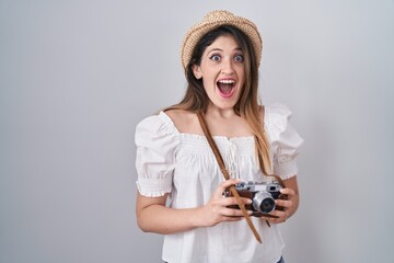 Sticker - Young brunette woman holding vintage camera celebrating crazy and amazed for success with open eyes screaming excited.