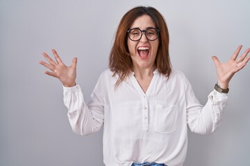 Sticker - Brunette woman standing over white isolated background celebrating crazy and amazed for success with arms raised and open eyes screaming excited. winner concept