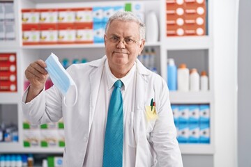 Poster - Middle age grey-haired man pharmacist smiling confident holding medical mask at pharmacy