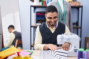 Wall Mural - Young arab man tailor smiling confident using sewing machine at clothing factory