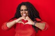© Krakenimages.com - Plus size hispanic woman standing over red background smiling in love doing heart symbol shape with hands. romantic concept.