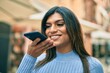 © Krakenimages.com - Young hispanic woman sending a voice message with smartphone at the town