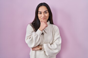 Poster - Young south asian woman standing over pink background looking confident at the camera smiling with crossed arms and hand raised on chin. thinking positive.