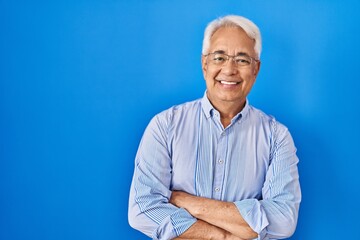 Wall Mural - Hispanic senior man wearing glasses happy face smiling with crossed arms looking at the camera. positive person.