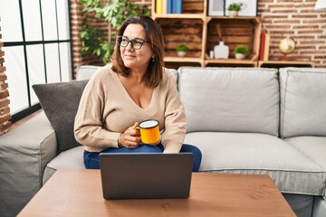 Sticker - Middle age hispanic woman using laptop and drinking coffee at home