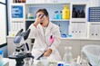 © Krakenimages.com - Hispanic girl with down syndrome working at scientist laboratory peeking in shock covering face and eyes with hand, looking through fingers with embarrassed expression.