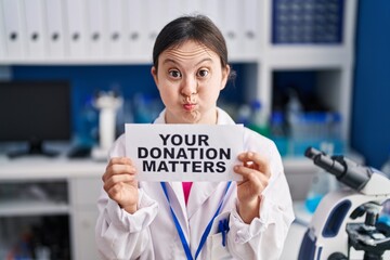 Poster - Woman with down syndrome working at scientist laboratory holding your donation matters banner puffing cheeks with funny face. mouth inflated with air, catching air.