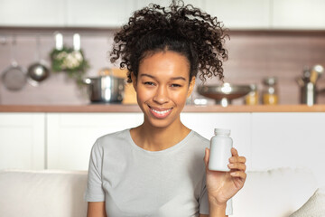 Happy young African American woman holding bottle of dietary supplements or vitamins in her hands. Close up. Healthy lifestyle concept