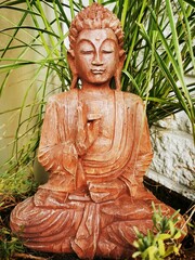 Canvas Print - Vertical shot of a wooden Buddha sculpture near green plants