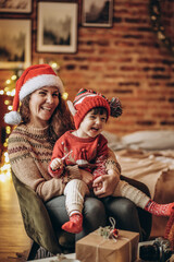 Happy baby with mother sit in armchair on christmas eve and kid eats christmas candy.