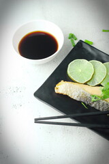 1 piece of salmon served in Japanese style in a black plate at a Japanese restaurant.