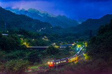 At Night, A Train With Lights Moves Through The Forest In The Mountains. A Small Train Station In The Mountain Forest.. Wanggu Railway Station, Pingxi District, New Taipei City. Taiwan