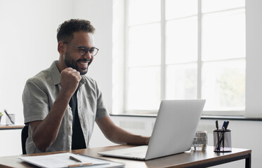 happy young businessman looking at laptop computer in office, excited african american man working a