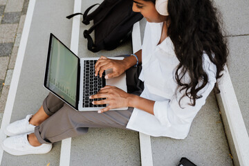 Young woman using laptop and headphones while studying outdoors