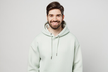 Young smiling cheerful fun cool happy satisfied positive optimist unshaven caucasian man wear mint hoody look camera isolated on plain solid white background studio portrait. People lifestyle concept.