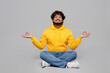 Full body spiritual young Indian man 20s he wear casual yellow hoody sit hold spreading hands in yoga om aum gesture relax meditate try to calm down isolated on plain grey background studio portrait.