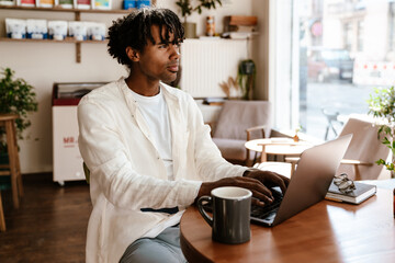 Young african man working on laptop while sitting in cafe