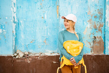 Thoughtful Young Woman With Yellow Backpack Leaning On Blue Cracked Wall