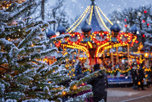 Christmas In Tivoli Gardens, Copenhagen, Denmark, With A Snow Covered Fir Tree In Front Of A Defocussed Carrousel Ride