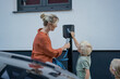 © Westend61 - Boy paying through credit card by mother holding electric car charger plug in front yard