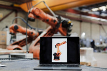 Laptop With Robotic Arm Photograph At Desk In Industry