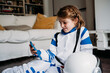© Westend61 - Girl wearing space costume looking at smart phone sitting in living room