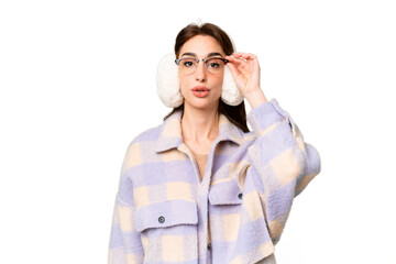 Young caucasian woman wearing winter muffs over isolated chroma key background with glasses and surprised