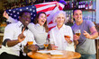 © JackF - Excited diverse soccer fans with American flag rejoicing winning game with glasses of beer in the pub