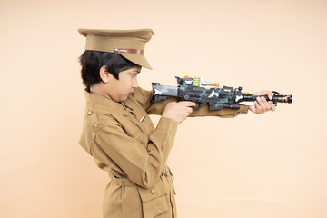 Indian boy kid wearing police custom dress holding gun in hand shooting at aim posing isolated on beige studio background. Closeup