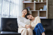 © ArLawKa - Young beautiful Asian LGBT lesbian happy couple sitting on sofa using smartphone in living room at home. LGBT lesbian couple living together