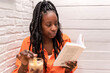 © Renata Hamuda - an African-American woman with braids having a drink while reading a book