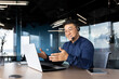 Leinwanddruck Bild - Asian with a headset is talking on video call, man inside office smiling and gesturing joyfully in an online meeting, a businessman is telling his colleagues, a customer service tech support worker.