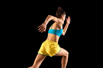 Wall Mural - Young sportive woman, runner and jogger in motion action isolated on black background. Sport, fitness, energy, movements concept