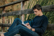 © ADDICTIVE STOCK - Young man sitting on wooden bridge reading book
