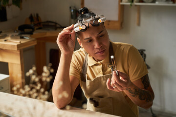 Wall Mural - Portrait of female jeweler holding gem with tweezers while creating custom art pieces