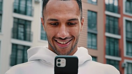 Emotional happy latino man blogger handsome african american guy sportsman buyer shopper stand in city use mobile phone apps chatting online reading text message browsing internet communication remote