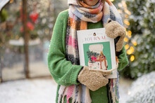 Woman Holding Magazine With New Year's Cover At Snowy Backyard Decorated For A Winter Holidays. Concept Of Publishing Or Posters On New Year's Theme, Close-up