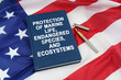 On the US flag lies a pen and a book with the inscription -PROTECTION OF MARINE LIFE, ENDANGERED SPECIES, AND ECOSYSTEMS