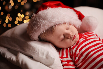 Canvas Print - Baby in Christmas pajamas and Santa hat sleeping on bed indoors