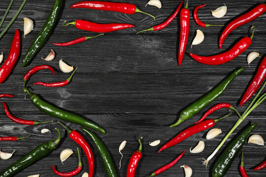 Frame of different chili peppers and garlic on black wooden table, flat lay. Space for text