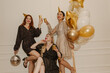 © Look! - Happy young interracial girls in sparkly dresses at bachelorette party raise paper cups indoors. Blonde, brunette and redhead with balloons and disco ball.