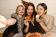 © Look! - Three young interracial best friends take selfie together eating pizza sitting on floor indoors. Girls wear sparkly dresses at party. Event concept