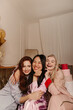 © Look! - Smiling young interracial girls laugh while hugging on sofa among gifts. Blonde, brunette and redhead wear pajamas at home. Friends concept