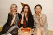 © Look! - Multicultural young women in evening dresses eating pizza at party sitting on floor indoors. Blonde, brunette and redhead are relaxing together. Holidays, celebration concept