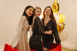 Three young interracial ladies smiling while looking at camera at party in elegant outfit indoors. Models celebrate new year, birthday together. Girlfriends concept